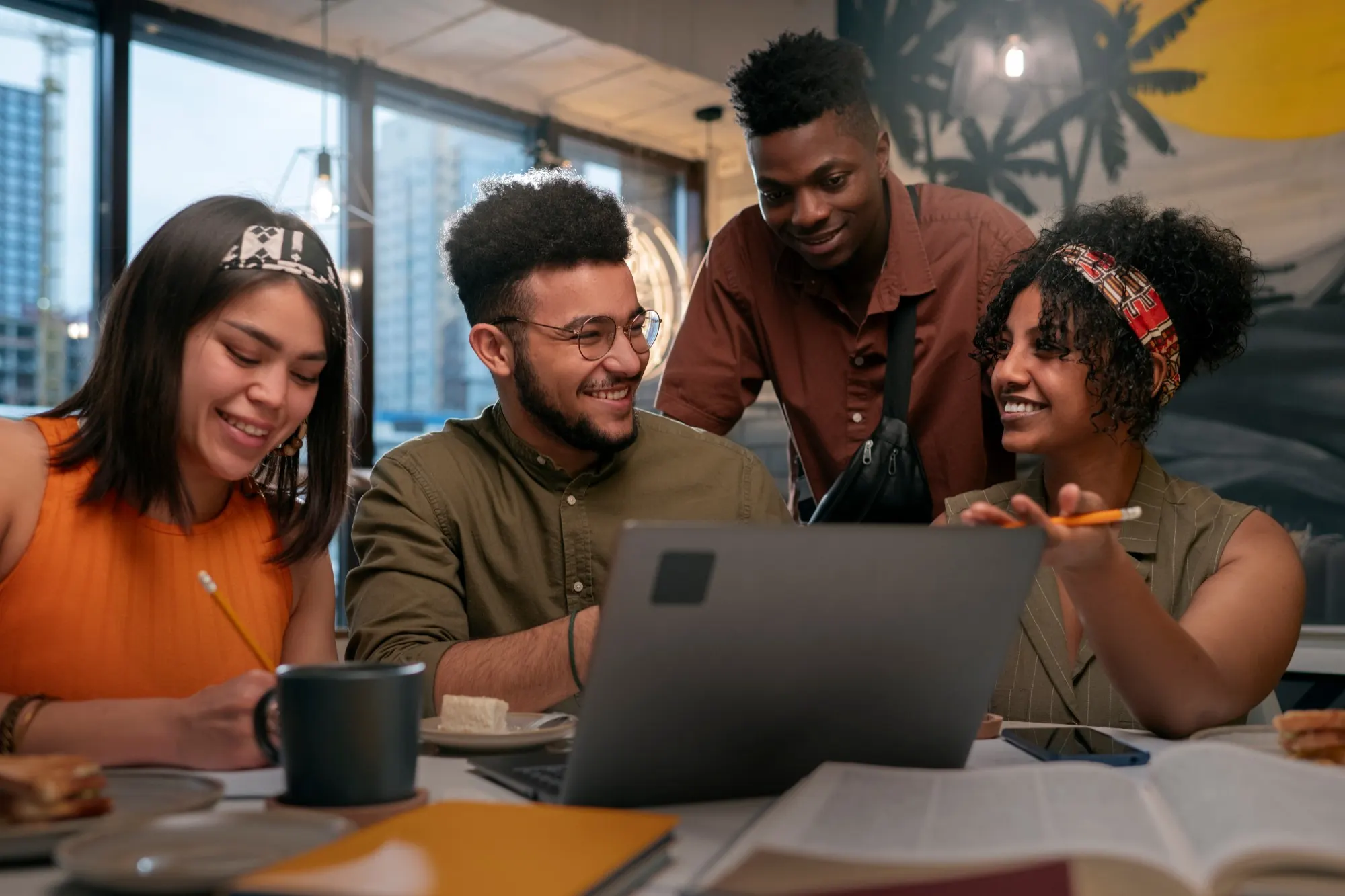 Quatro pessoas sorrindo enquanto trabalham juntas em volta de um notebook